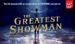 'The Greatest Showman' written over the top of an image of a man standing under a spotlight with his hands in the air