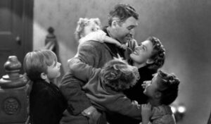 A black and white still of a man being embraced by his wife and children