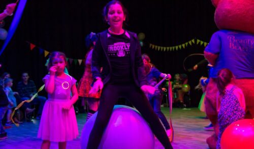 A girl standing over a bouncy hopper in the background families are playing at a family rave