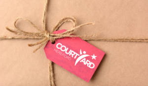 A brown paper present with a string bow tied around it. It has a red label with The Courtyard logo on it