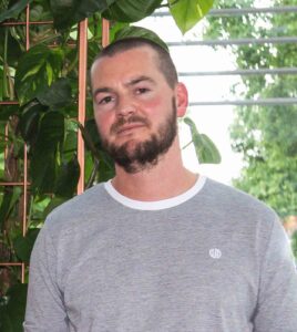 Dermot Clarke - a young man with short dark hair and a beard, wearing a grey tshirt