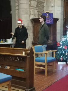 Two young adults perform in a church in front of a Christmas tree