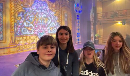 Four children standing in front of a Beauty and the Beast stage curtain