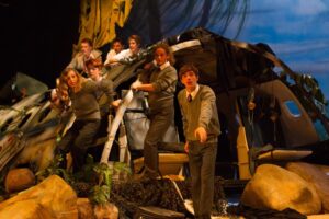 A group of young actors dressed in school uniforms on stage, performing in Lord Of The Flies