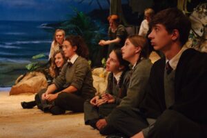 A group of young actors dressed in school uniforms on stage, performing in Lord Of The Flies