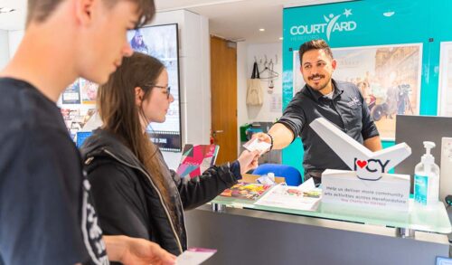A man leans over a Box Office counter handing tickets to two young people