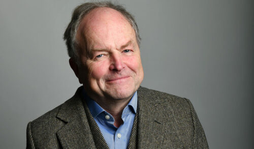 A close up of Clive Anderson smiling at the camera wearing a tweed jacket
