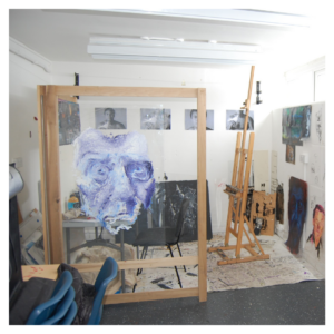 A picture of an artists studio. On the left is a blue portrait painted on glass. On the right is an easel. 