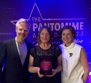 A man and two women stand smiling holding an award