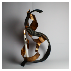 A sculpture formed of two pieces of intertwining metal holds a lit candle.