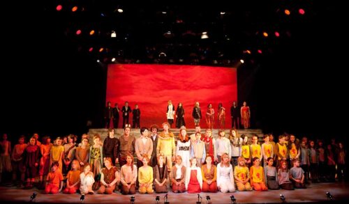 A cast of children on stage dressed in costumes for The Lion The Witch and The Wardrobe