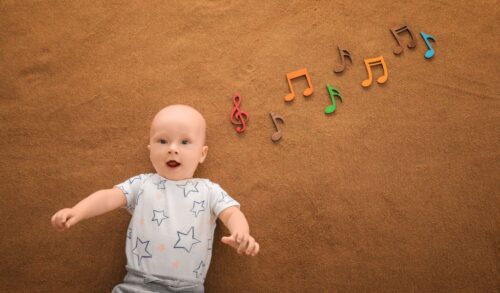 A baby lying against a brown background with colourful music notes to the side of it