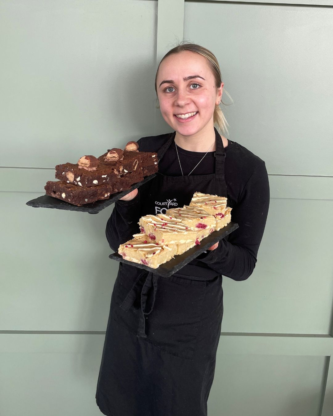 A girl smiling whilst holding two slates with cakes on