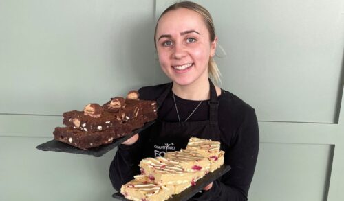A picture of a girl smiling whilst holding two slates with cakes on