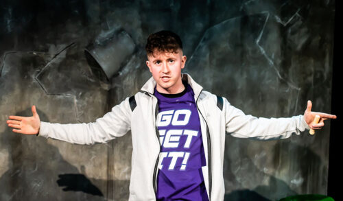 A boy wearing a purple top and white hoodie stands with his arms outstretched