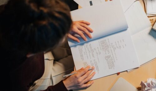 A birds eye view on a person sat at a desk holding a pencil with their hands on a script