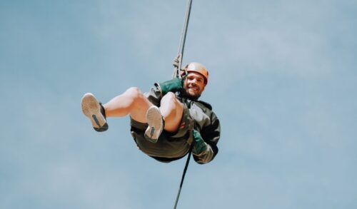 A man abseiling whilst smiling against a clear blue sky