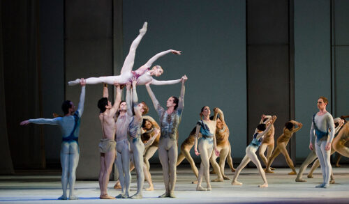 A group of dancers on stage dressed in leotards holding a female dancer above their heads