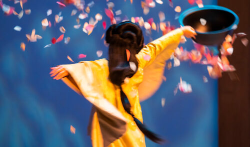 A woman with an elaborate hairstyle and dress spinning round in a circle throwing petals