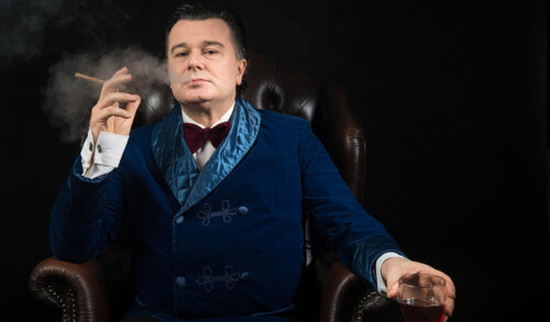 Image A distinguished gentleman sat in a leather chair smoking a cigar and holding a glass of brandy