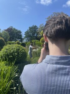A close up of a man taking a photo of a girl standing in a garden