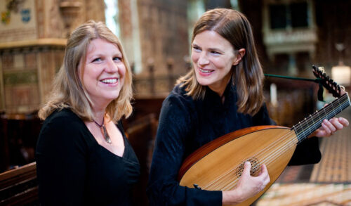 Two women smile inside a church One holds an old string instrument