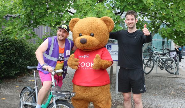 Phil Pearcy stood next to Cookie The Courtyard mascot and a man on a bike