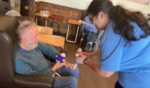 A girl holds knitted teddies out towards a care home resident
