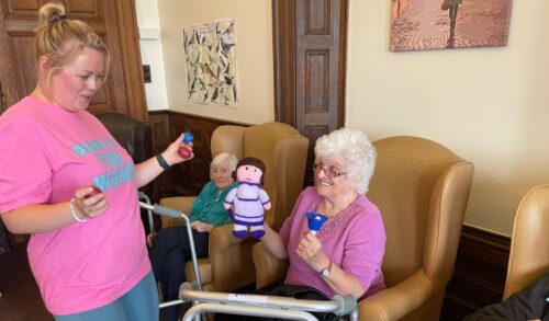 A workshop leader smiling with an elderly lady who holds two knitted dolls