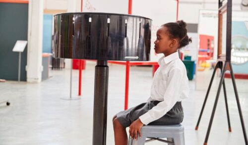 A girl sat in front of a zoetrope on a grey stool