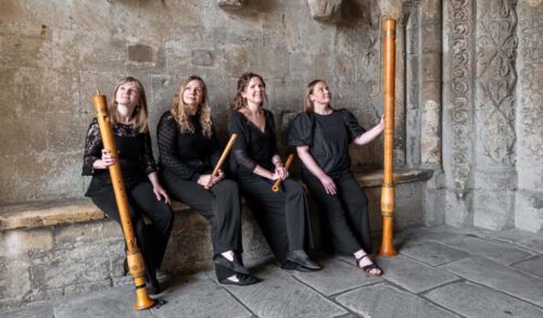 Four women sit on a stone bench holding woodwind instruments