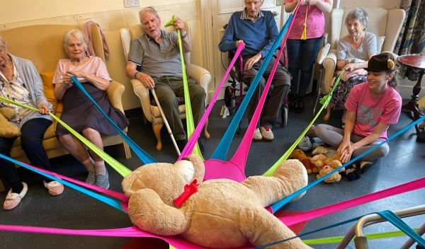 Residents in a care home holding a big teddy bear on a series of coloured ties