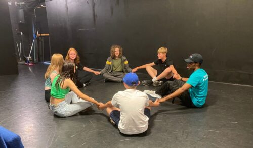 A group of young people sitting in a circle with a Youth Theatre leader