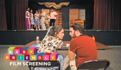 A man and a woman sit on chairs in front of a large stage On the stage stands a small group of children eagerly awaiting a response from the adults In the bottom left the text reads Baby Friendly Screening