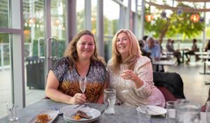 Two woman in sparkly dresses holding up prosecco glasses to the camera