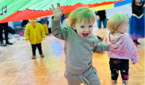 A little boy runs under a coloured parachute grinning