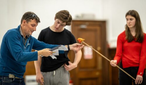 Three people in rehearsal One holding a script one looking at the script and one holding a long stick with a toy robin on the end