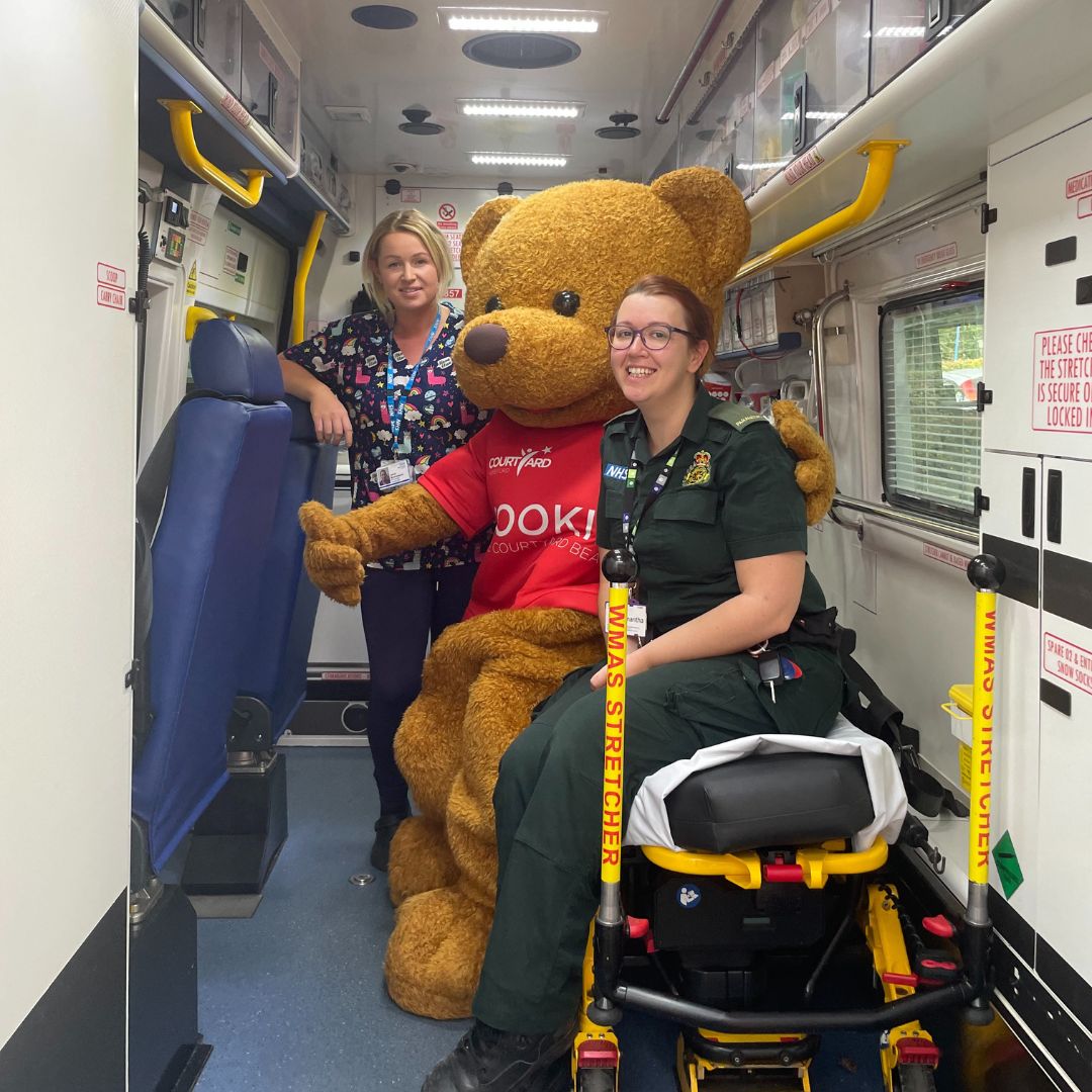 Cookie The Courtyard bear sitting in an ambulance with a paramedic and nurse