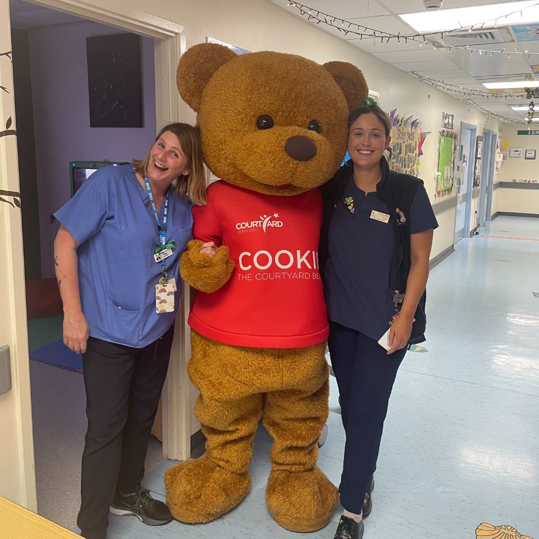 Cookie The Courtyard Bear standing on a hospital ward with two nurses