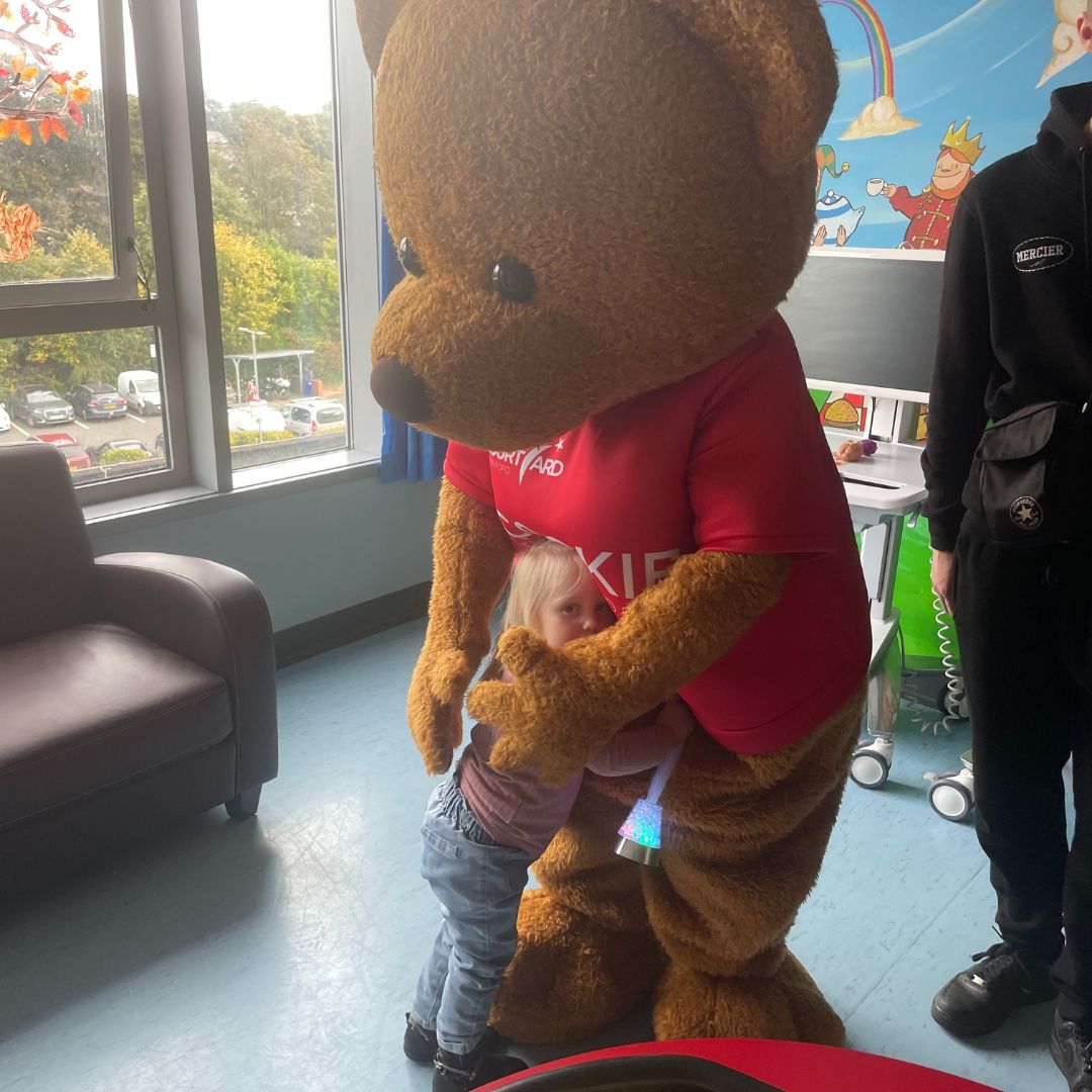 A young girl hugging Cookie The Courtyard Bear in a hospital ward