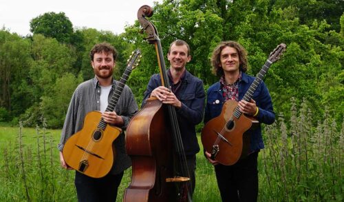 Three men holding string instruments smiling at the camera standing outside