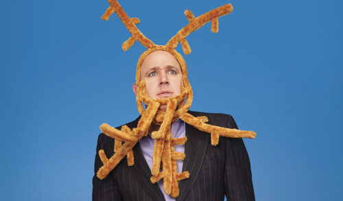 A man wearing a suit stands looking concerned His head is wrapped up in reindeer headbands that look like antlers