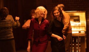 Two women, one blonde and one brunette, dance at an office party.