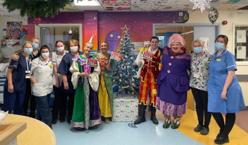 Cast members from Dick Whittington smiling alongside hospital staff by a Christmas tree