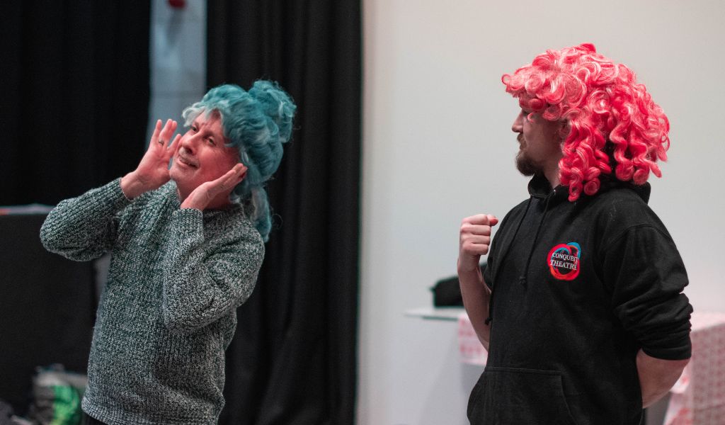 Two men in coloured wigs act alongside each other.