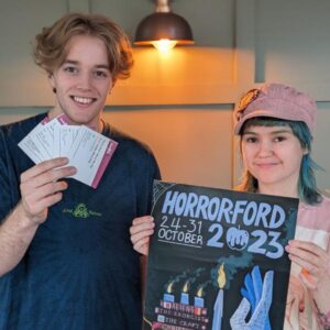 Our Young Film Programmers Finn and Georgia stand holding a poster that reads 'Horror-ford' and 4 tickets. 
