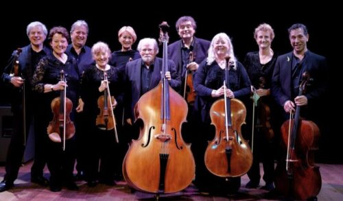 An image of a string orchestra smiling at the camera holding their instruments