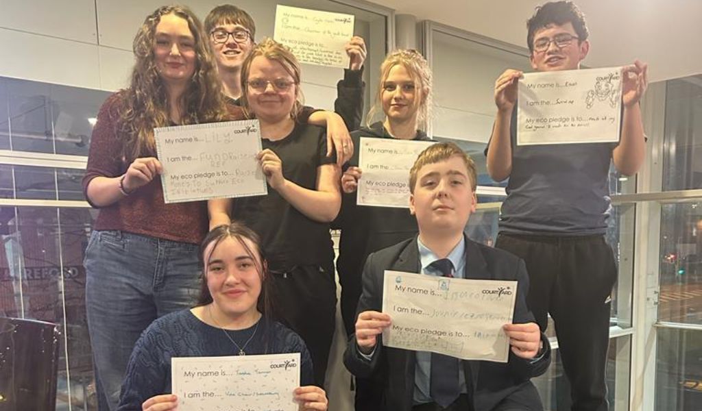 A group of young people smiling at the camera holding pieces of paper displaying eco pledges