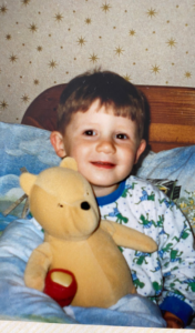A young boy sat smiling in bed holding a teddy bear