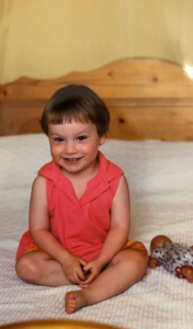 A young girl sitting cross legged on a bed smiling